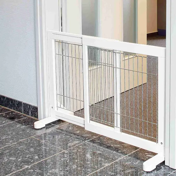 Barrera de seguridad para perros de color blanco con barrotes metálicos y pies de goma antideslizantes en un pasillo de baldosas.