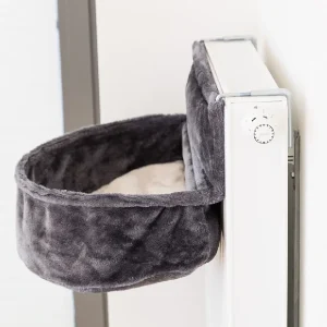 Bolsa de felpa para radiador en color gris, montada sobre un radiador blanco, ideal para que los perros pequeños disfruten de un lugar cálido y confortable en casa.