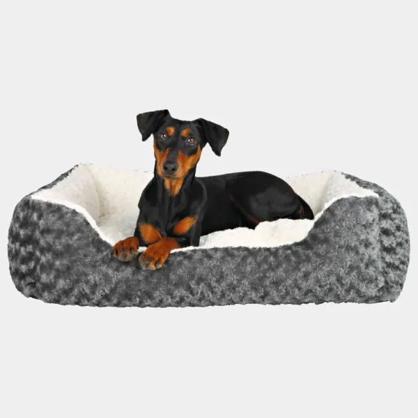 Perro pequeño de raza doberman pinscher tumbado en una cama de felpa para perros en tonos grises y blancos, mostrando confort y diseño ergonómico