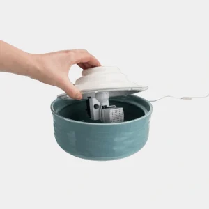 Montaje de la Fuente Automática de Cerámica Trixie Vital Falls Mano ensamblando la fuente automática de cerámica Trixie Vital Falls, mostrando su mecanismo interno y la facilidad de instalación para proporcionar agua fresca y filtrada a las mascotas