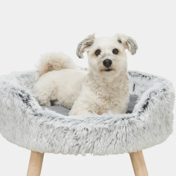 Perro pequeño y blanco disfrutando de un cómodo sofá para mascotas con felpa de pelo largo gris y patas de madera naturales