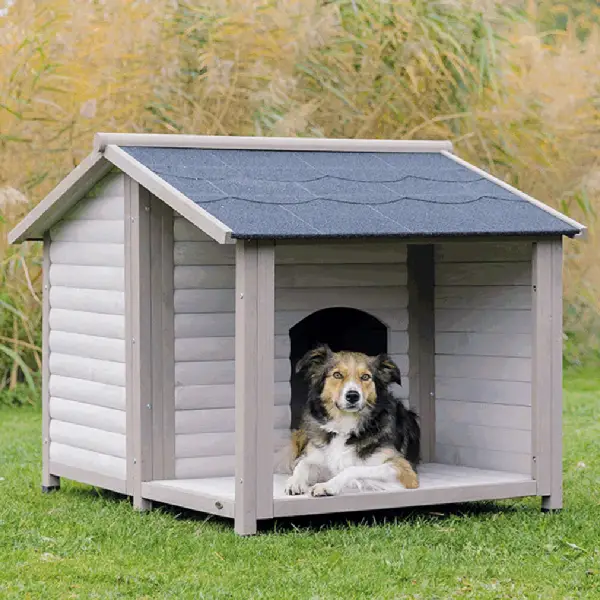 Perro descansando en una caseta para perros de madera resistente al clima con techo a dos aguas, situada en un entorno natural