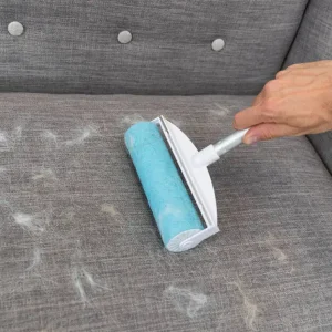 Rodillo Quitapelusas de Perro Eficaz para Sofás y Telas Uso práctico del rodillo quita pelusas de perro en sofá gris, eliminando eficientemente el pelo de mascota