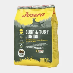 Pienso sin Cereales para Perros Josera Surf & Turf Junior 900g Bolsa de 900g de Pienso sin Cereales para Perros Josera Surf & Turf Junior, enfocado en cachorros de razas medianas y grandes con proteína de cordero y salmón, etiquetado como libre de cereales y con certificación de calidad en un fondo forestal que evoca la naturaleza