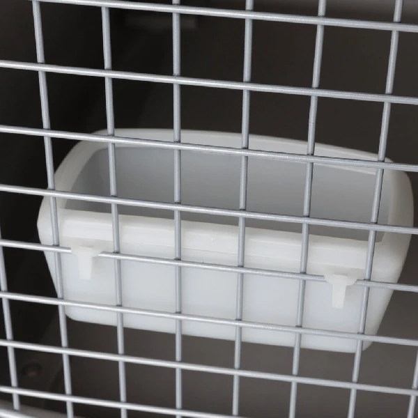 Detalle de un comedero de plástico blanco acoplable a un transportín de coche para perros, mostrando su facilidad de acceso y uso seguro a través de la puerta de rejilla metálica.