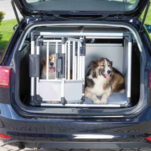 Dos perros grandes, uno dentro de una jaula transportadora de aluminio y otro al lado, cómodamente situados en el maletero de un coche, demostrando el ajuste espacioso y seguro de la jaula transportadora para viajes
