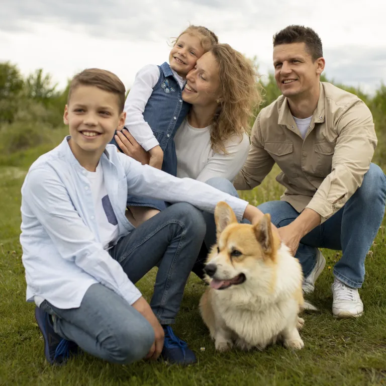 Familia al aire libre acompañada de un perro Corgi, ejemplificando la armonía entre mascotas y niños en el hogar